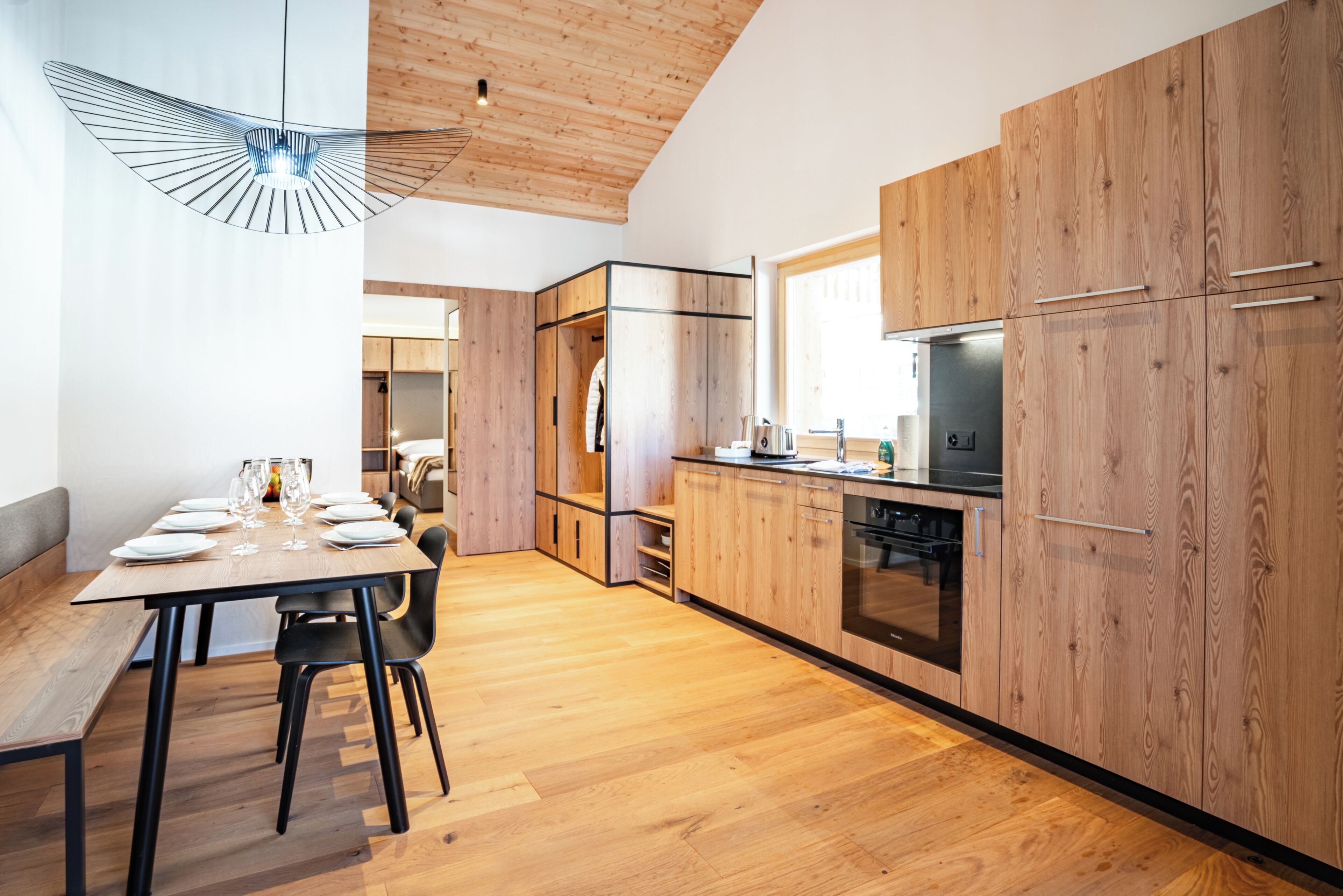 A modern kitchen with wooden cabinets, a built-in oven, and a dining area with a bench and chairs.