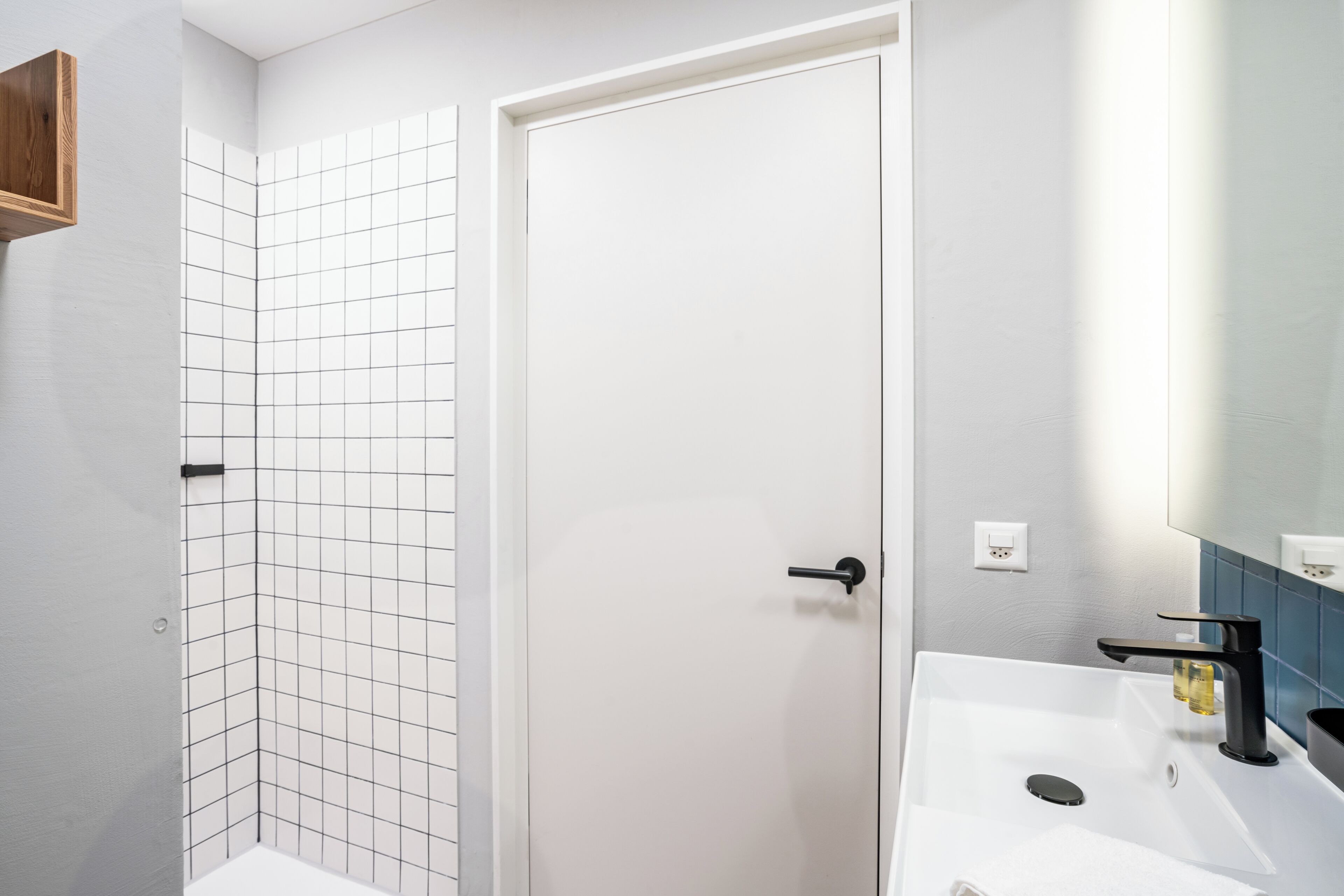 A bathroom with a white sink, a mirror, and a shower area with white tiles.