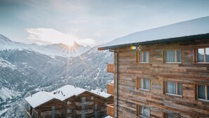 Une cabane en bois dotée de plusieurs balcons, entourée de montagnes enneigées et surplombant un ciel dégagé.