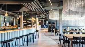 Un espace bar moderne, doté de tabourets, d’un comptoir et d’un coin salon avec des tables et des chaises.