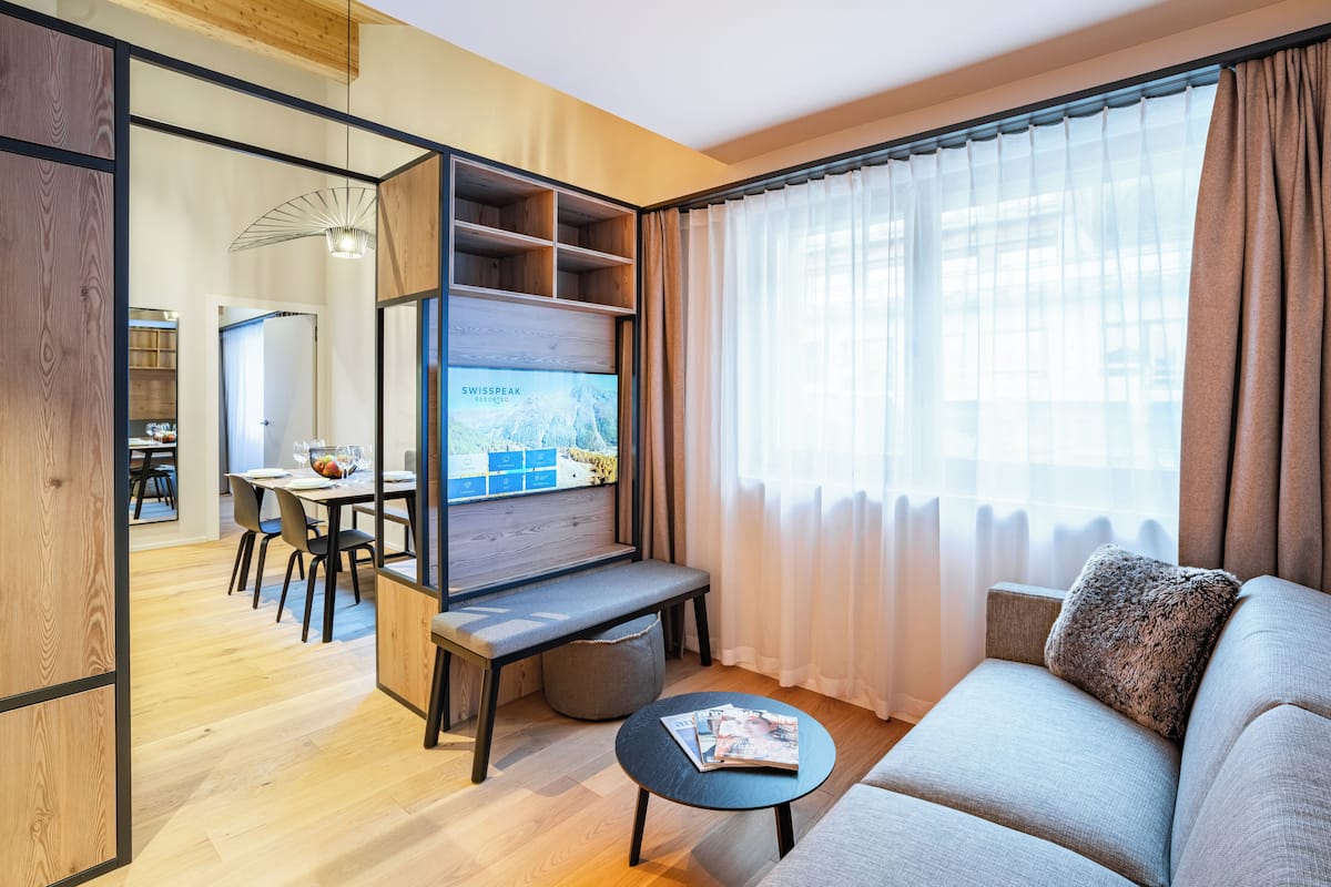 A modern living room with a sofa, a coffee table, a TV, and a dining area with chairs and a table.