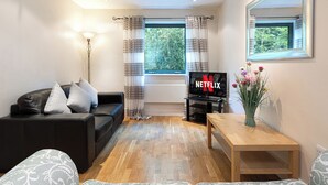 A living room with a black sofa, a wooden coffee table, a TV with the Netflix logo, a window with curtains, and a vase with flowers. -  Quayside Newcastle (Newcastle upon Tyne)