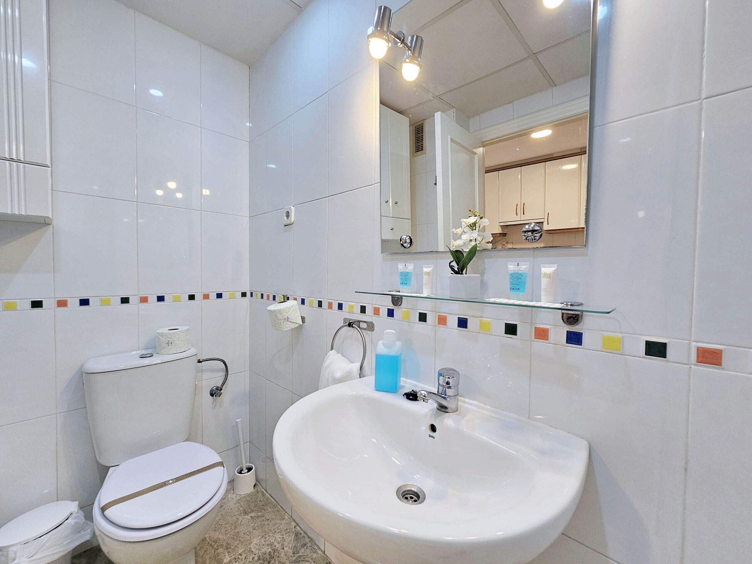 A modern bathroom with white tiles, a large sink, a toilet, and a mirror.