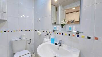 A modern bathroom with white tiles, a large sink, a toilet, and a mirror.