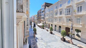 Une rue bordée d’immeubles à l’architecture riche, avec un trottoir pavé et des plantes en pot.