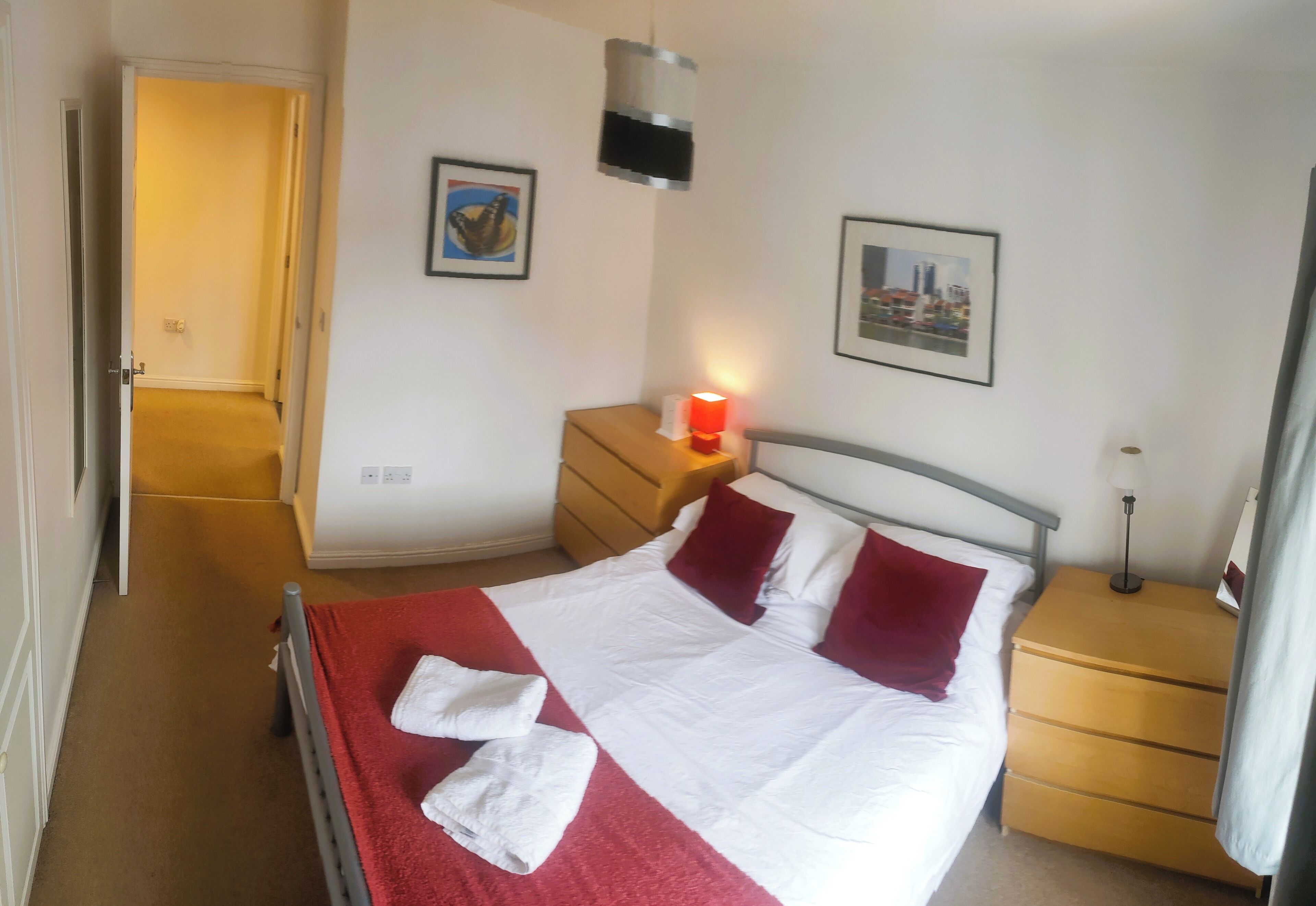 A hotel room with a bed, a nightstand, a lamp, a door, and a wall with two framed pictures.
