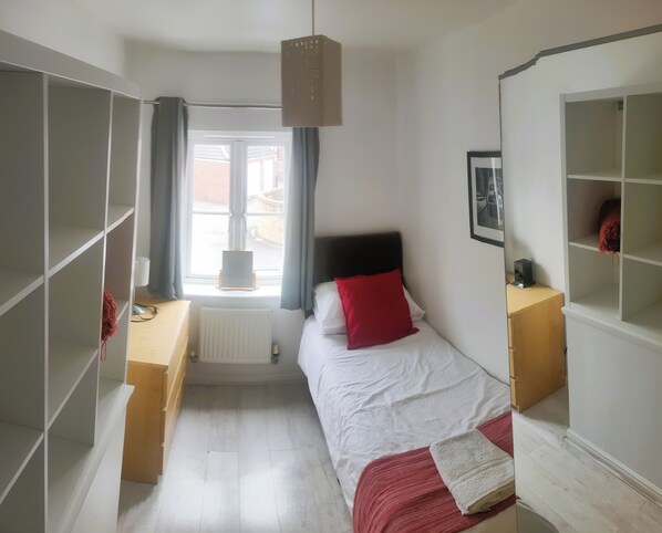 A bedroom with a bed, a radiator, a window with curtains, a hanging light fixture, and a wardrobe. - Landau House (Bristol)