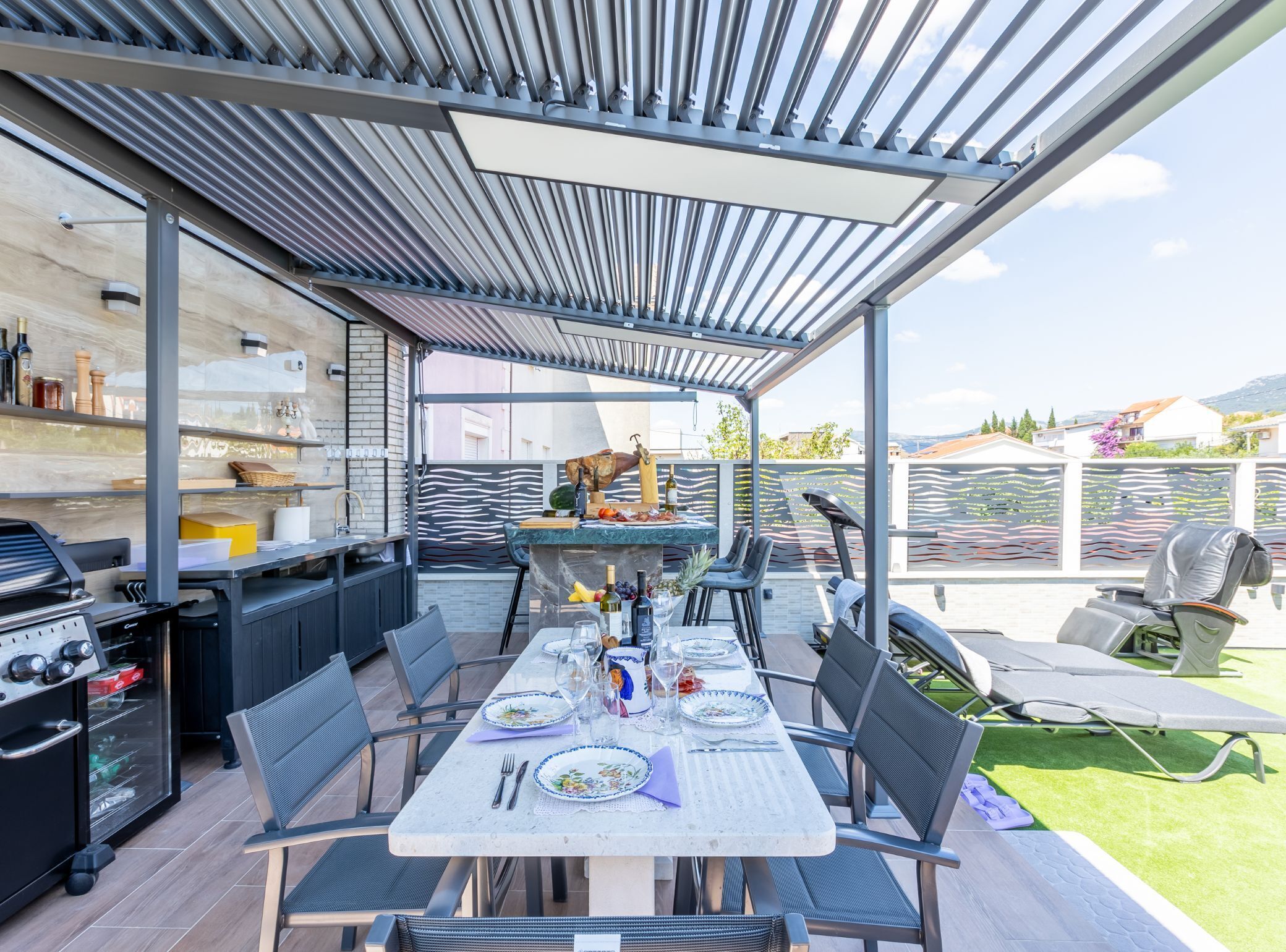 An outdoor patio with a covered dining area, a grill, and a view of the surrounding landscape.
