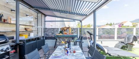 An outdoor patio with a covered dining area, a grill, and a view of the surrounding landscape.