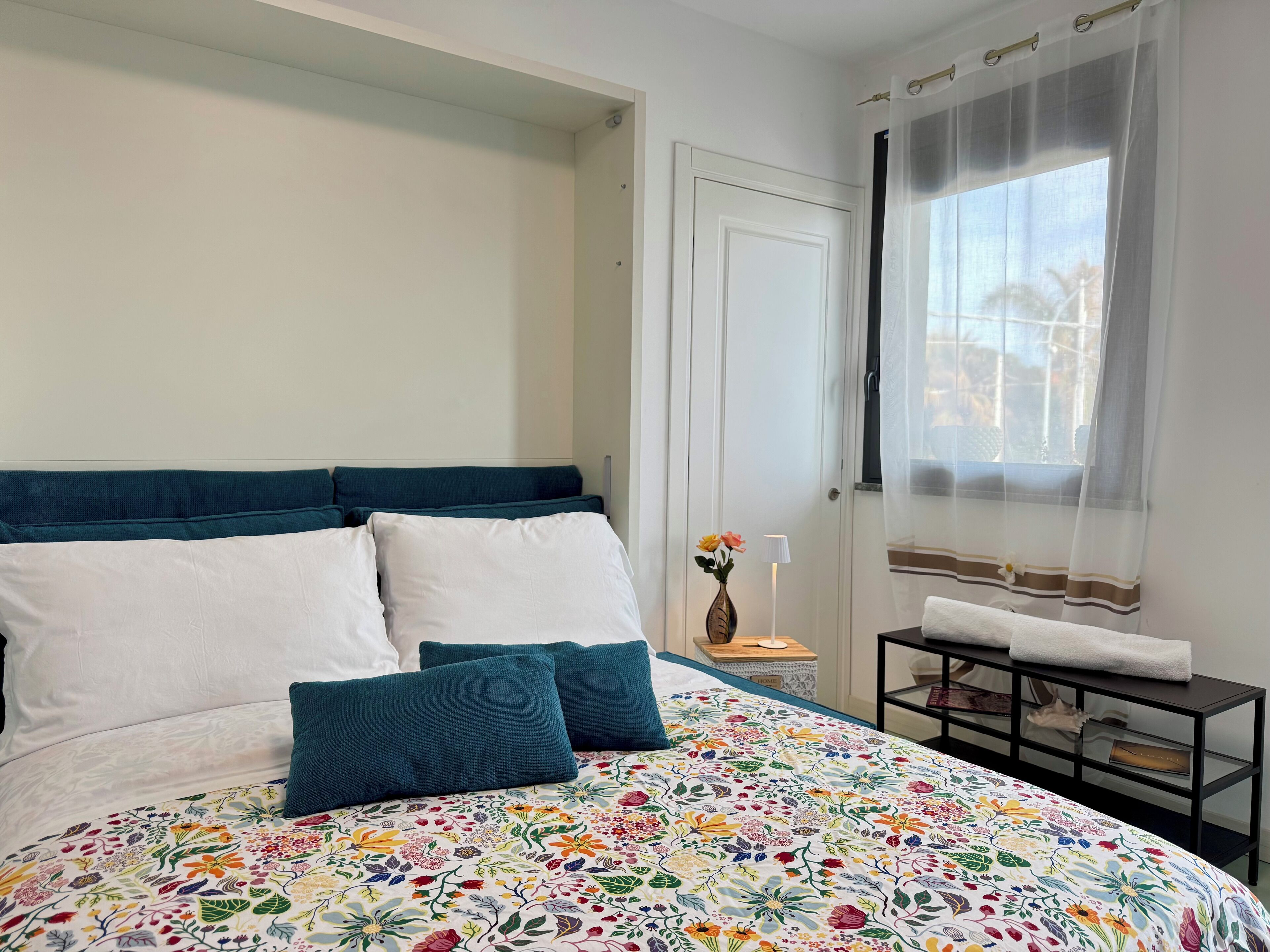 A bedroom with a bed, a nightstand, a window with curtains, and a door.