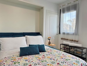 A bedroom with a bed, a nightstand, a window with curtains, and a door. - Aurora View Resort - Boutique Suites (Mascali)