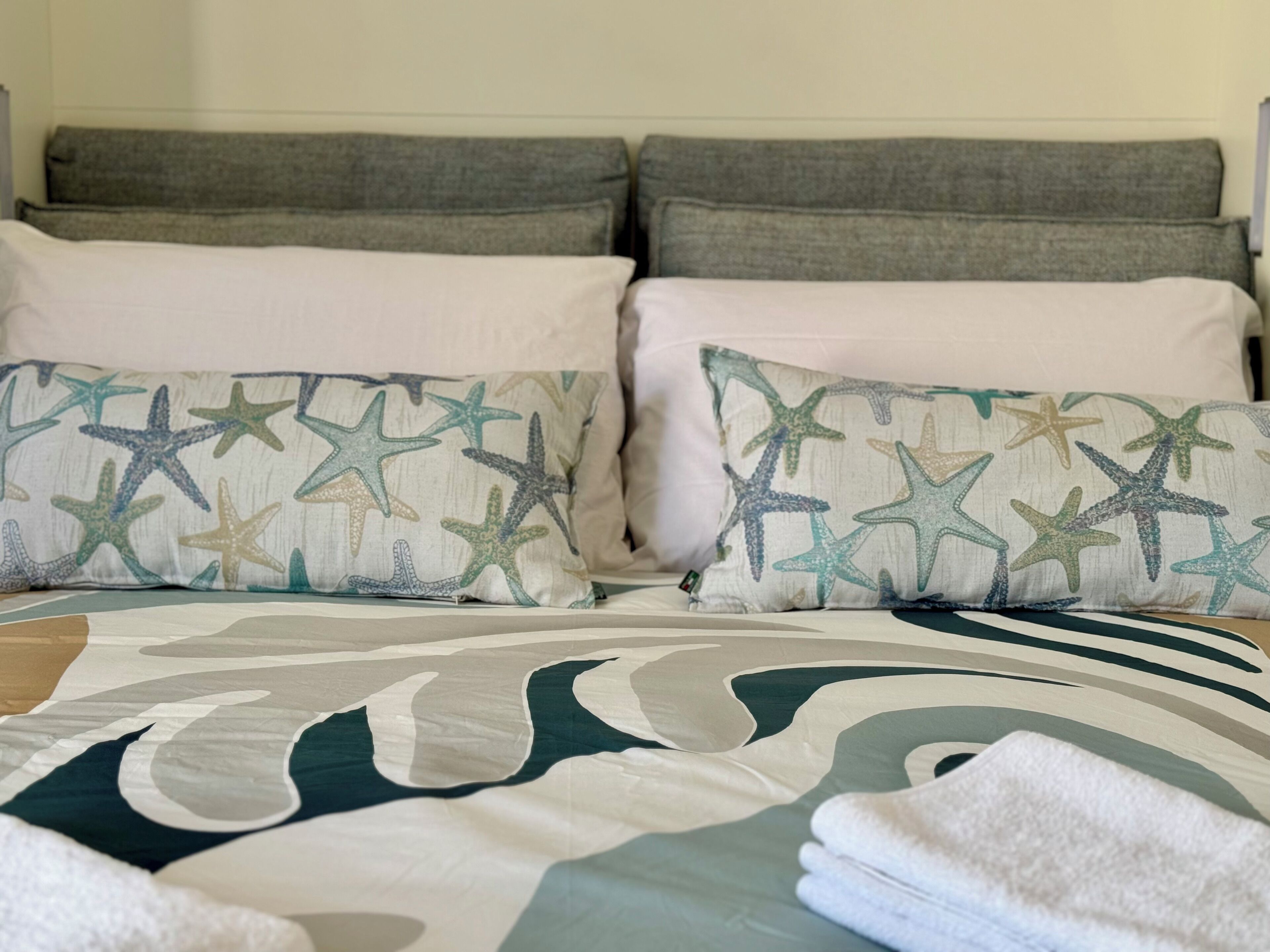 A bed with a patterned pillow, a large decorative pillow, and a folded towel.