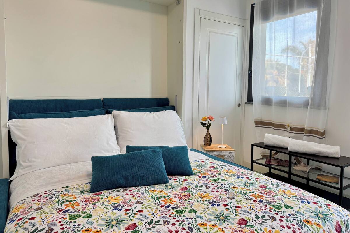 Una cama con colcha estampada, almohadas turquesa y cabecero blanco.