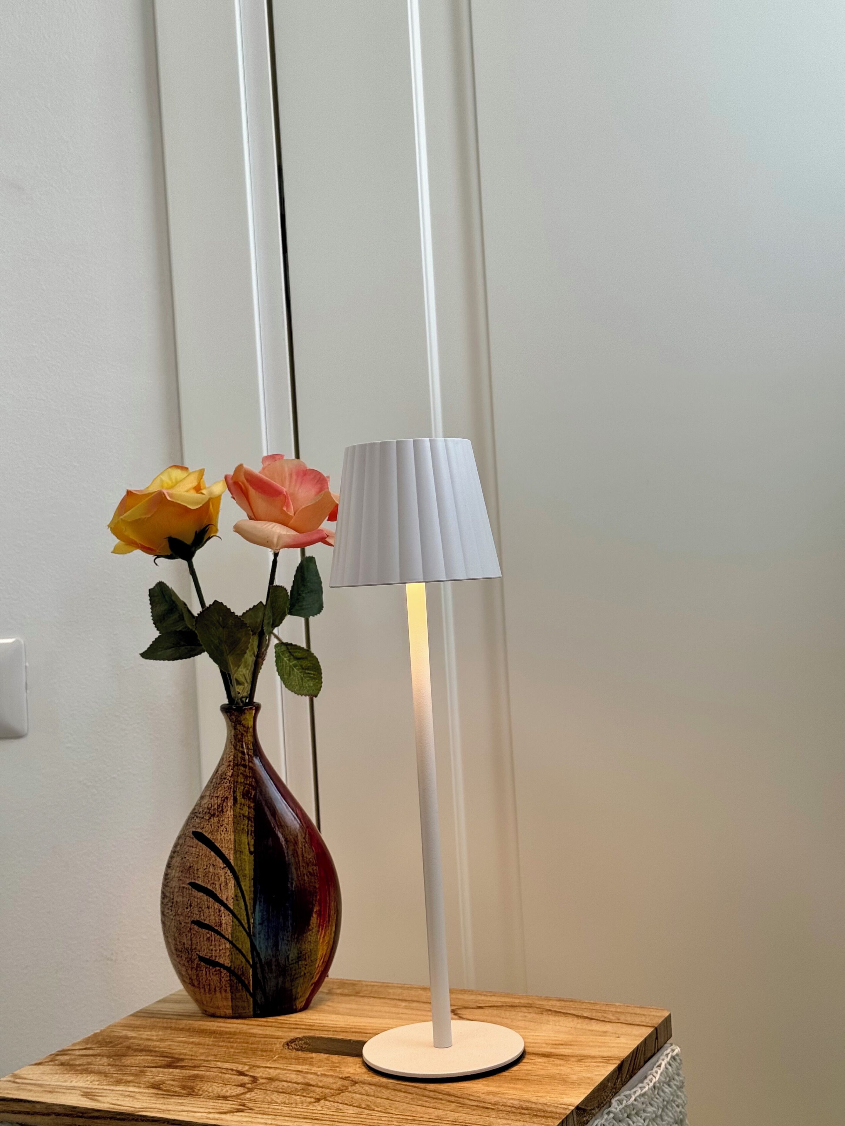 Ein Holztisch mit einer Vase, die zwei Rosen enthält, und einer weißen Stehlampe.