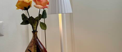 Ein Holztisch mit einer Vase, die zwei Rosen enthält, und einer weißen Stehlampe.