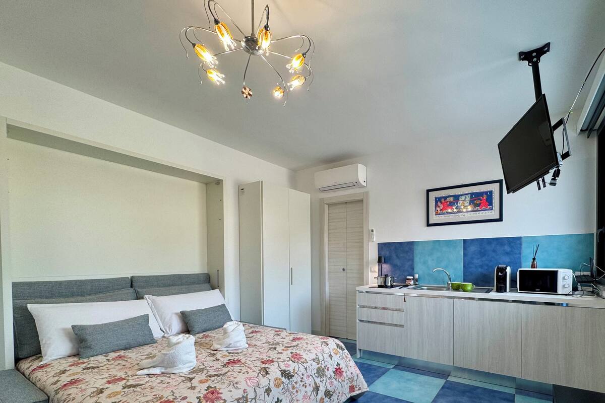 Un dormitorio moderno con cama, mesitas de noche, armario, kitchenette y una lámpara en el techo.
