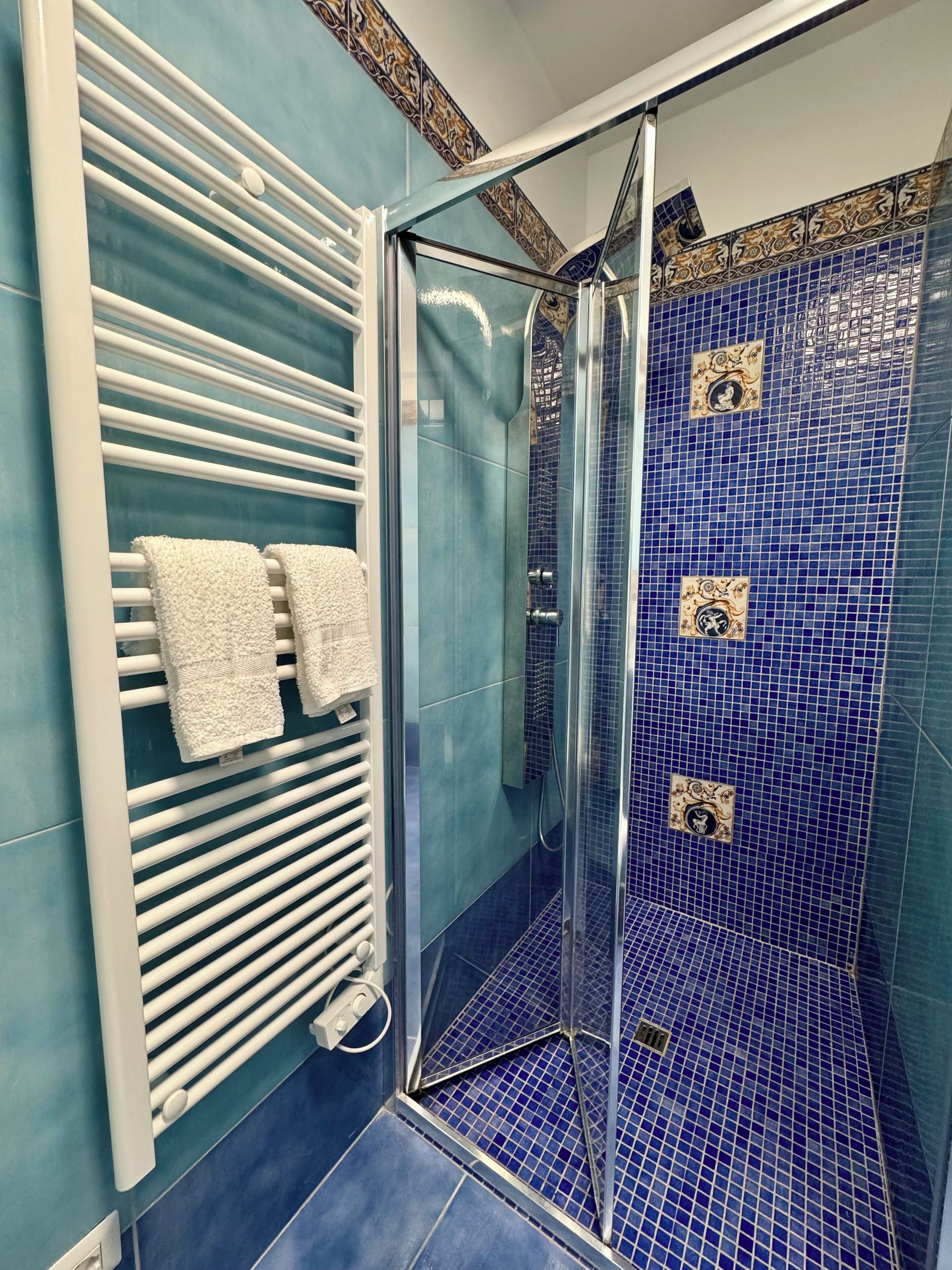 A bathroom with a glass shower enclosure, a white towel rack, and blue-tiled walls.