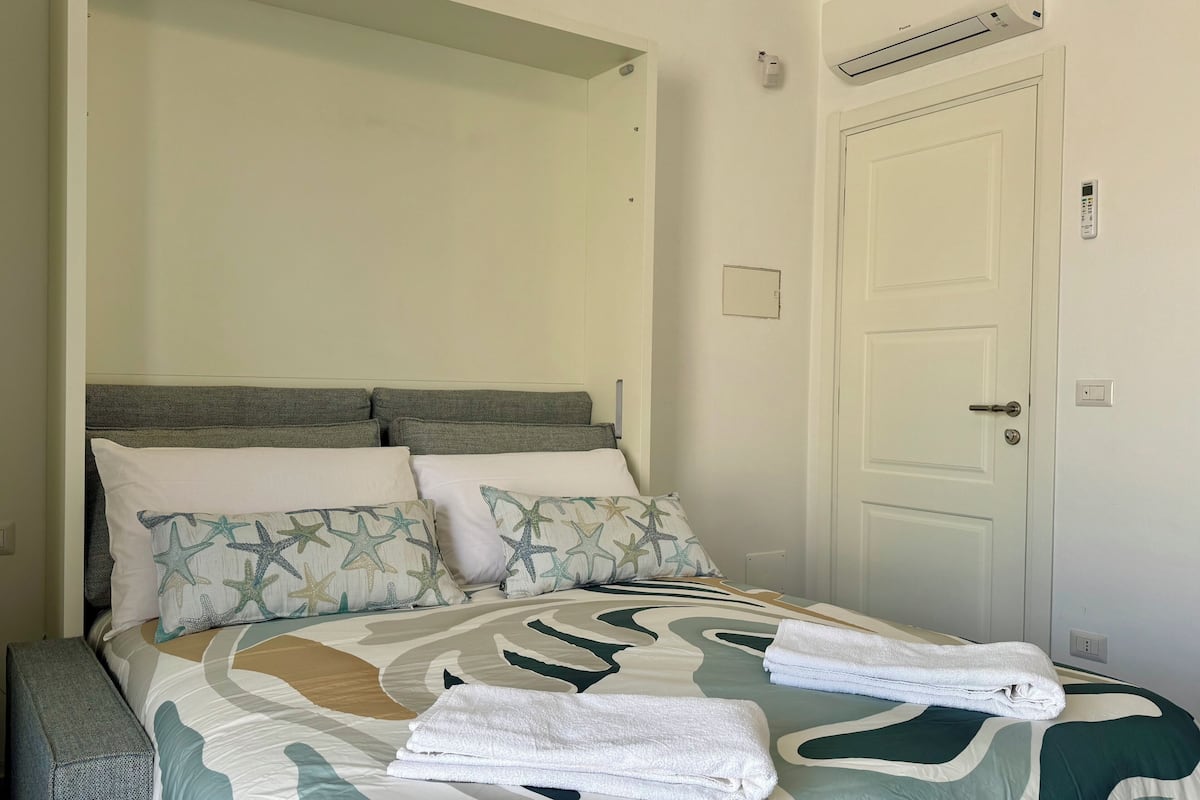 Una cama bien hecha con una colcha estampada, dos almohadas con motivos de estrellas de mar y dos toallas dobladas.