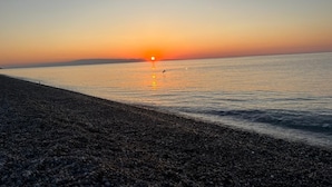 A pebbled beach with a sunset over the water. - Aurora View Resort - Boutique Suites near Taormina & Mount Etna (Mascali)
