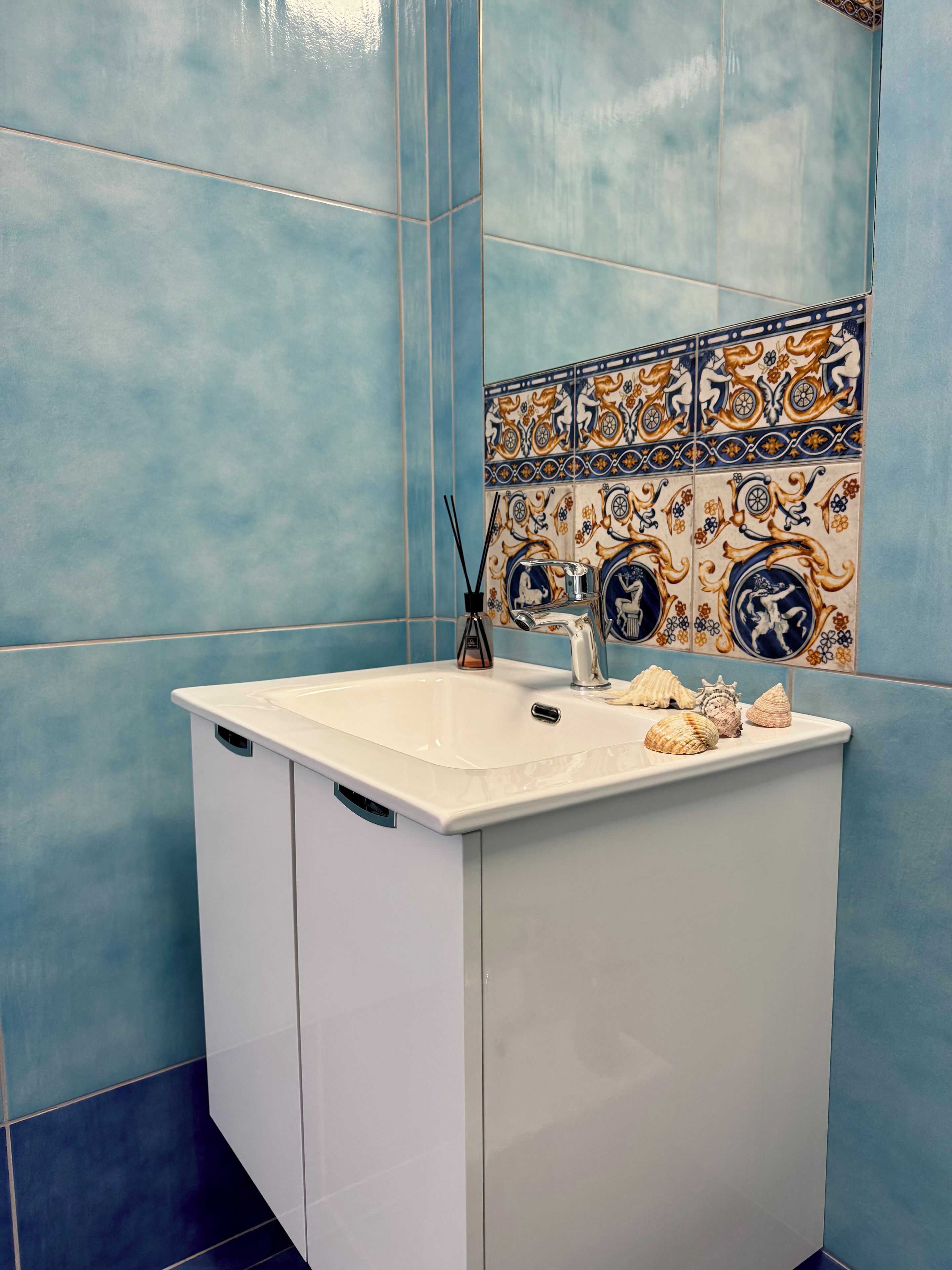 Un baño con un lavamanos blanco, azulejos azules y azulejos decorativos sobre el lavamanos.