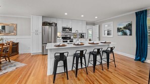 Une cuisine moderne avec des meubles blancs, des appareils en acier inoxydable et un îlot central doté de tabourets de bar.