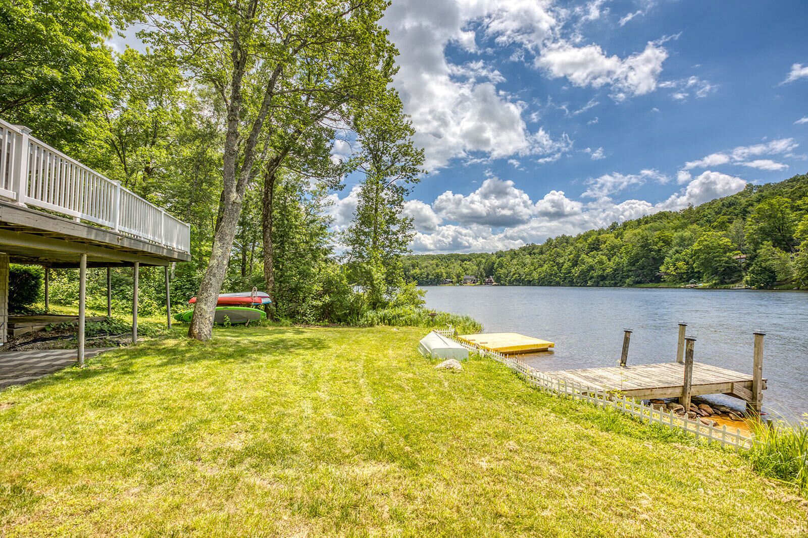 A lakeside property with a wooden deck, a covered area, and a dock with a boat.