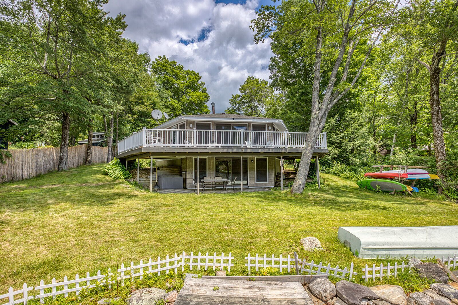 A two-story house with a balcony, surrounded by a white picket fence, and a grassy yard.