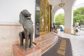 Une statue de lion se trouve à l’entrée d’un bâtiment dont le sol est recouvert de carreaux et la porte est ornée d’un portail doré.