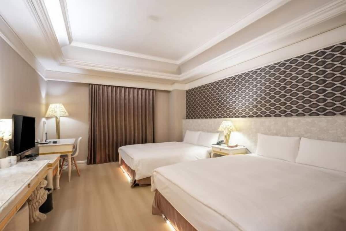 Habitación de hotel con dos camas, un escritorio con televisor, una lámpara y un papel tapiz estampado.