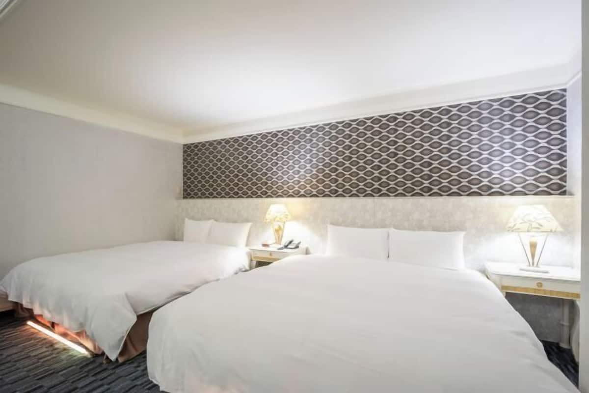 Habitación de hotel con dos camas, cabecera estampada, lámparas de noche y suelo alfombrado.