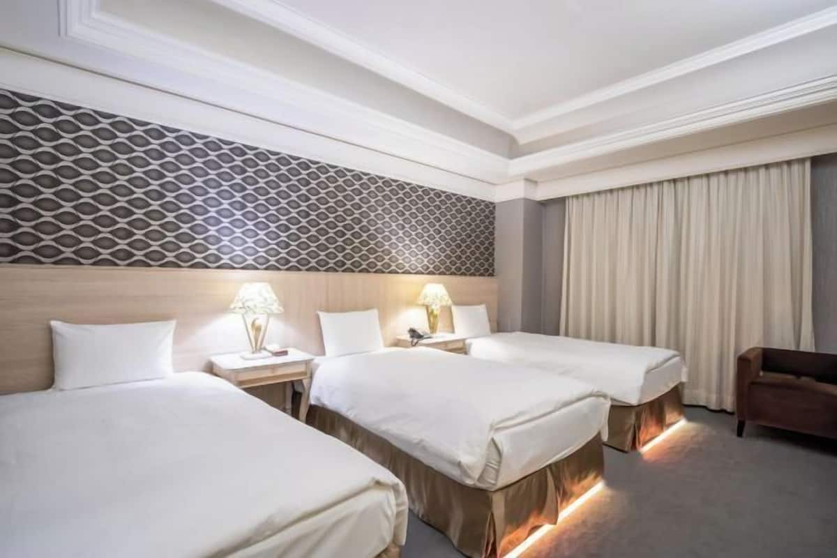 Una habitación de hotel con tres camas, un papel tapiz estampado y un ventanal grande con cortinas.