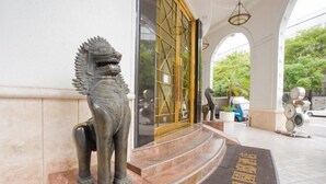 Una estatua de bronce de un león en la entrada de un edificio, con suelo de baldosas y una puerta de vidrio con marco dorado.