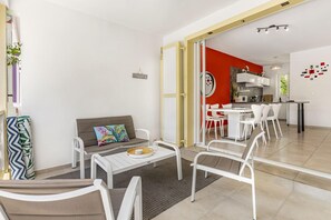 A modern living room with a sofa, coffee table, and chairs, a kitchen area with white appliances, and a red accent wall.