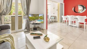 A modern living room with a TV, white furniture, a dining area with white chairs, and a red accent wall. - Villa 6p private pool   Orient Bay Beach (Community of Saint Martin)