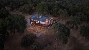 Una casa con paneles solares, rodeada de árboles, y una terraza con luces.