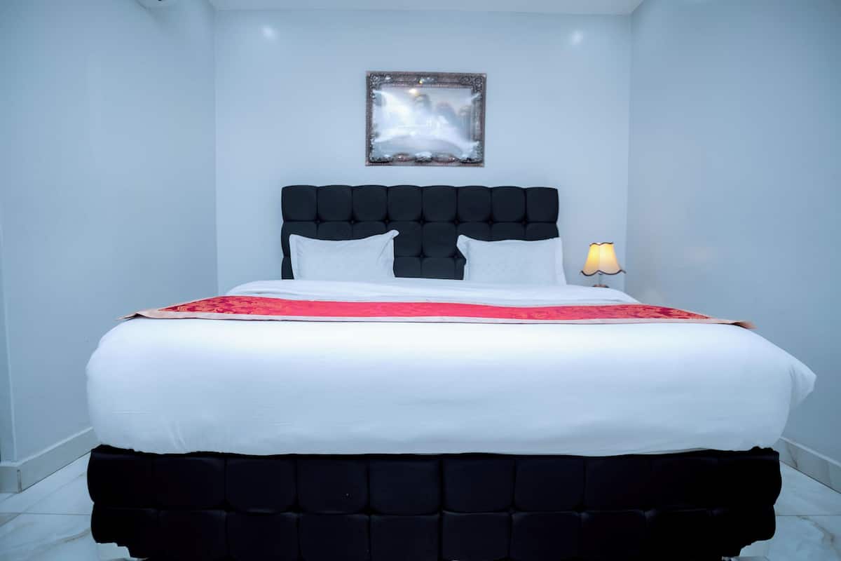 A neatly made bed with a black headboard, white bedding, and a red accent.