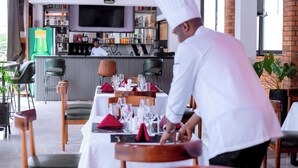 A restaurant with a bar area, tables set with red napkins, and a chef in uniform.
