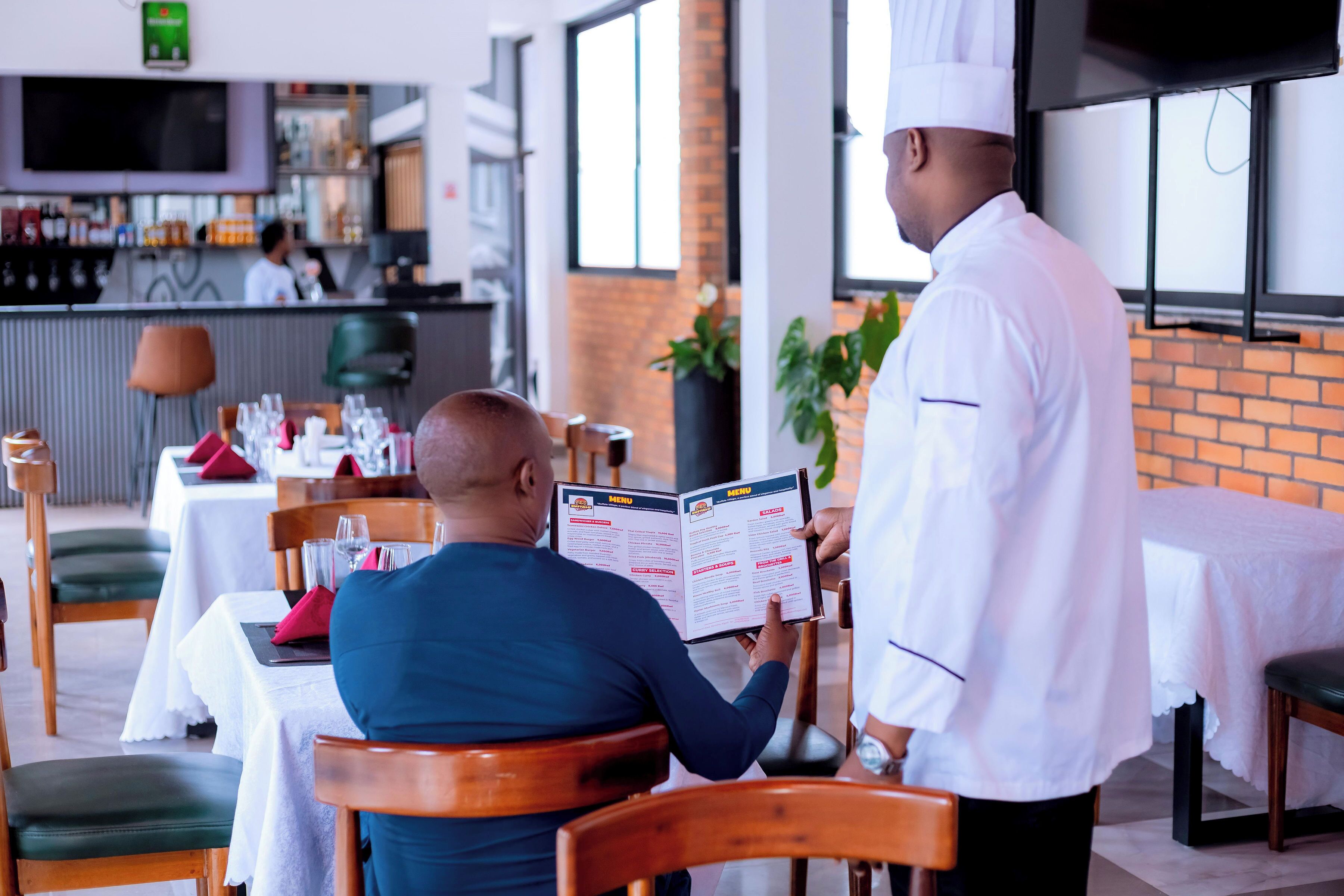 A restaurant interior with tables, chairs, a menu stand, and a bar area in the background.