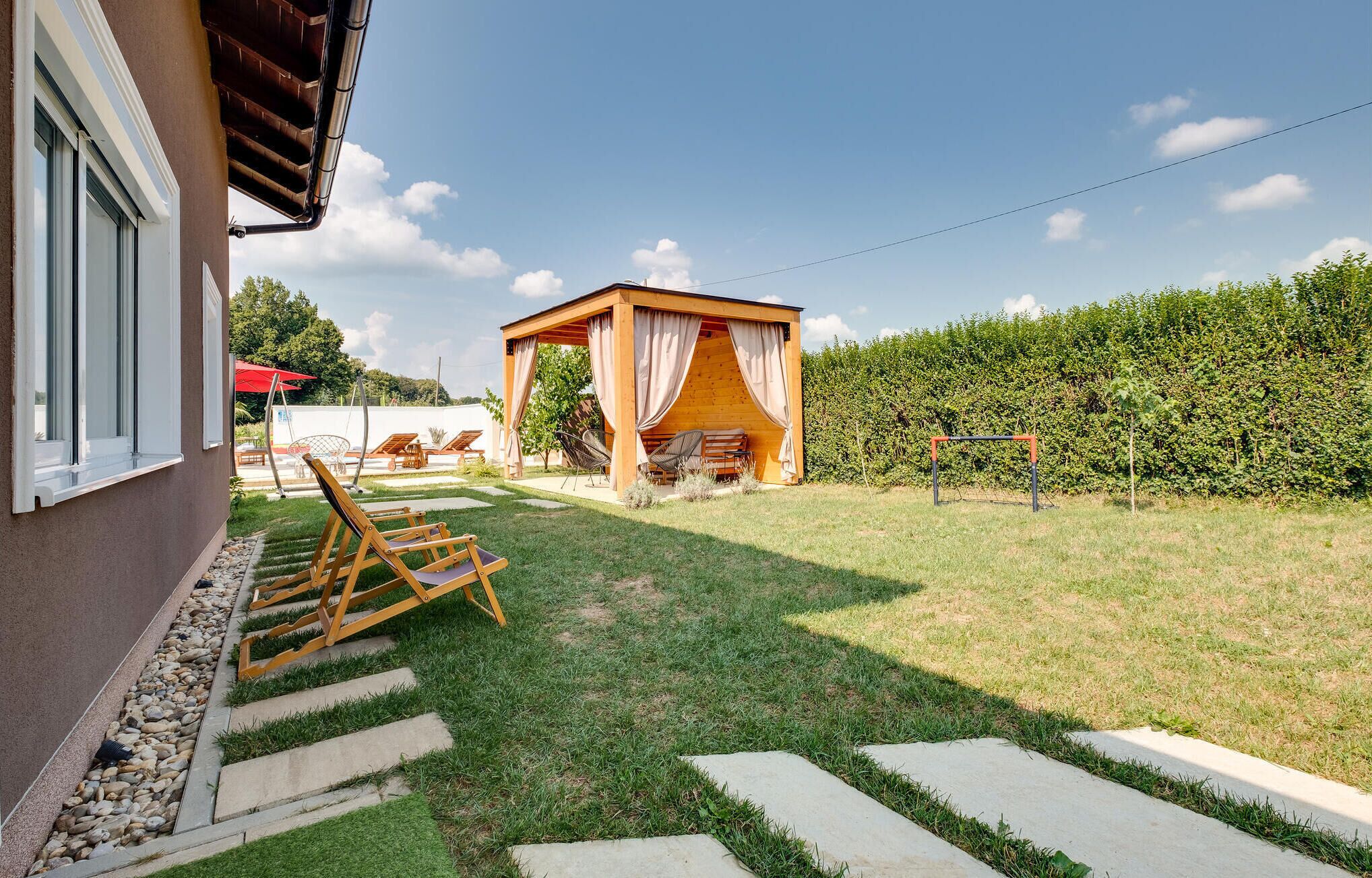 Een achtertuin met een houten pergola, een kleine houten schuur en een zithoek met stoelen en een tafel.