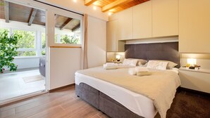 Un dormitorio con una cama grande, vigas de techo de madera, un gran ventanal corredero que da a un balcón y vistas a la vegetación exterior.