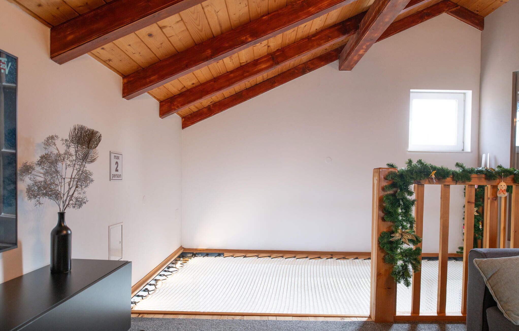 A room with a sloped ceiling, a tatami mat floor, a wooden bench with a garland, and a small window.