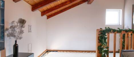 A room with a sloped ceiling, a tatami mat floor, a wooden bench with a garland, and a small window.