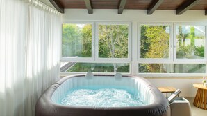 Un jacuzzi en una habitación con ventanas grandes que dan a un jardín.