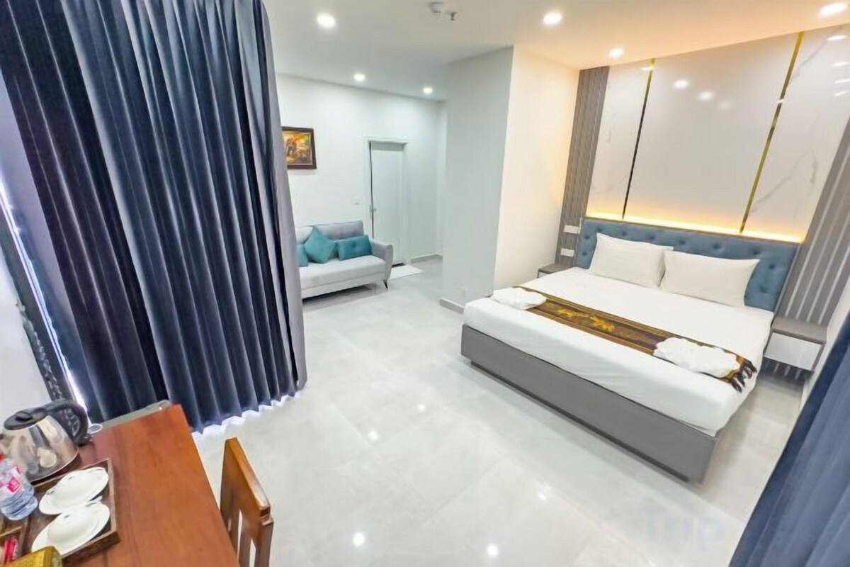 A modern hotel room with a large bed, a dining area, and a separate seating area.