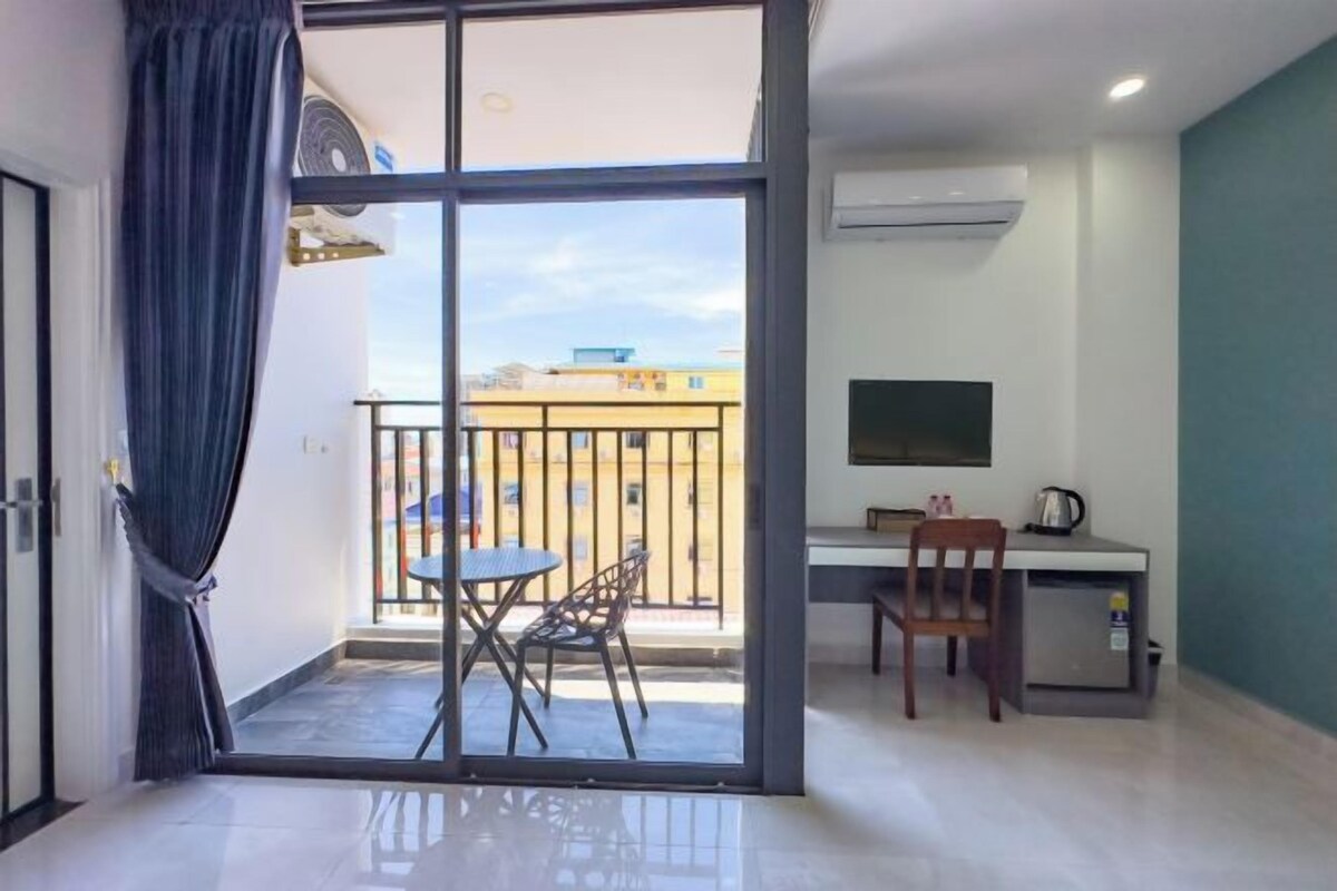 Une chambre dotée d’une porte-fenêtre coulissante donnant sur un balcon, d’un bureau avec une chaise et d’un téléviseur fixé au mur.