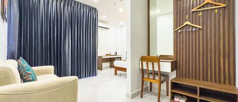 A modern hotel room with a sofa, a desk, a chair, a large mirror, and a wardrobe with a shoe rack.