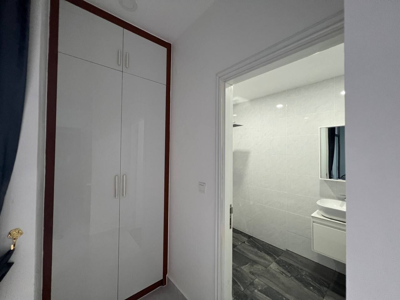Een hal met een witte kast, een witte wastafel en een spiegel in een badkamer.