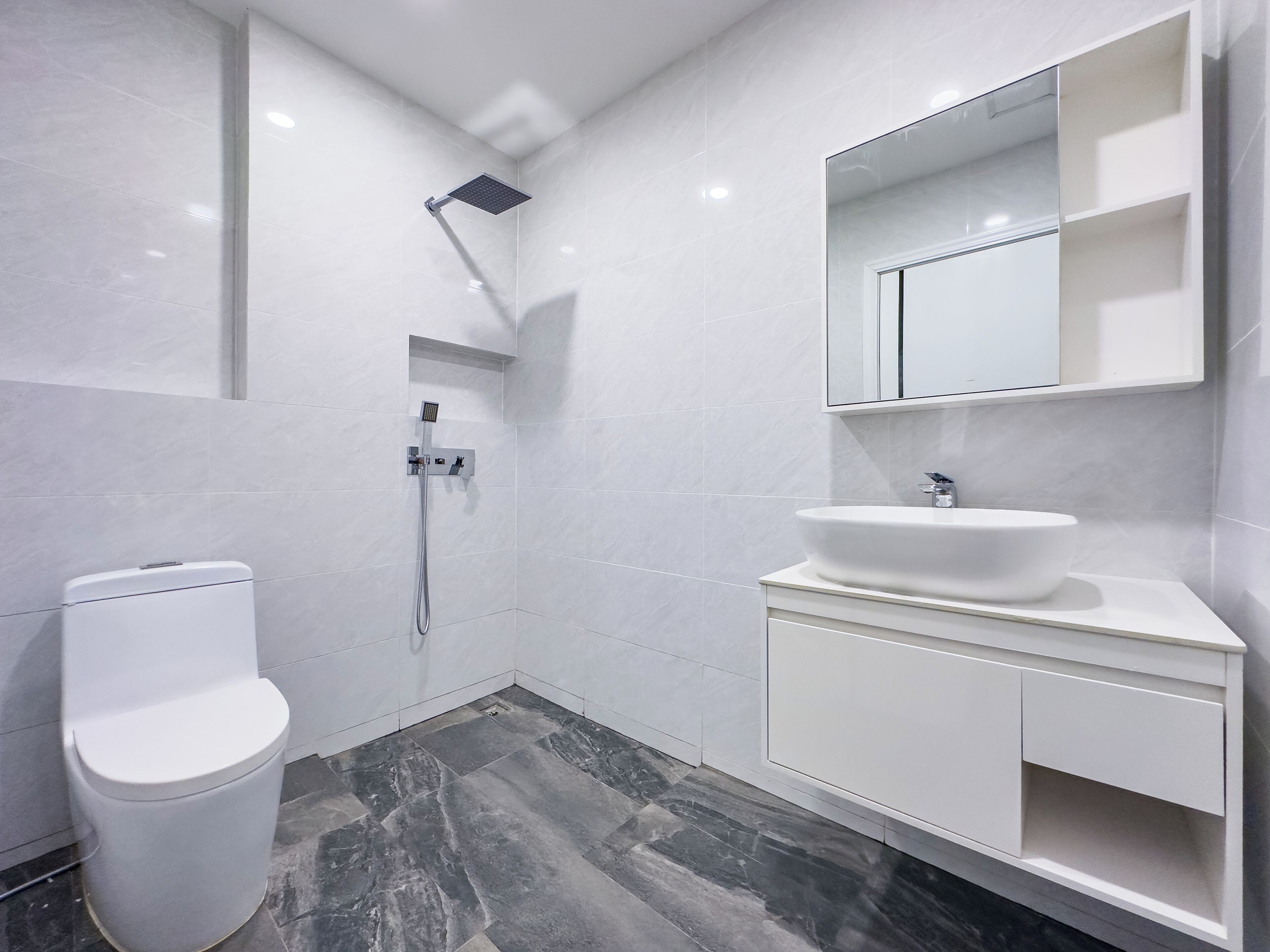 Un baño moderno con inodoro blanco, un lavabo grande y una ducha.