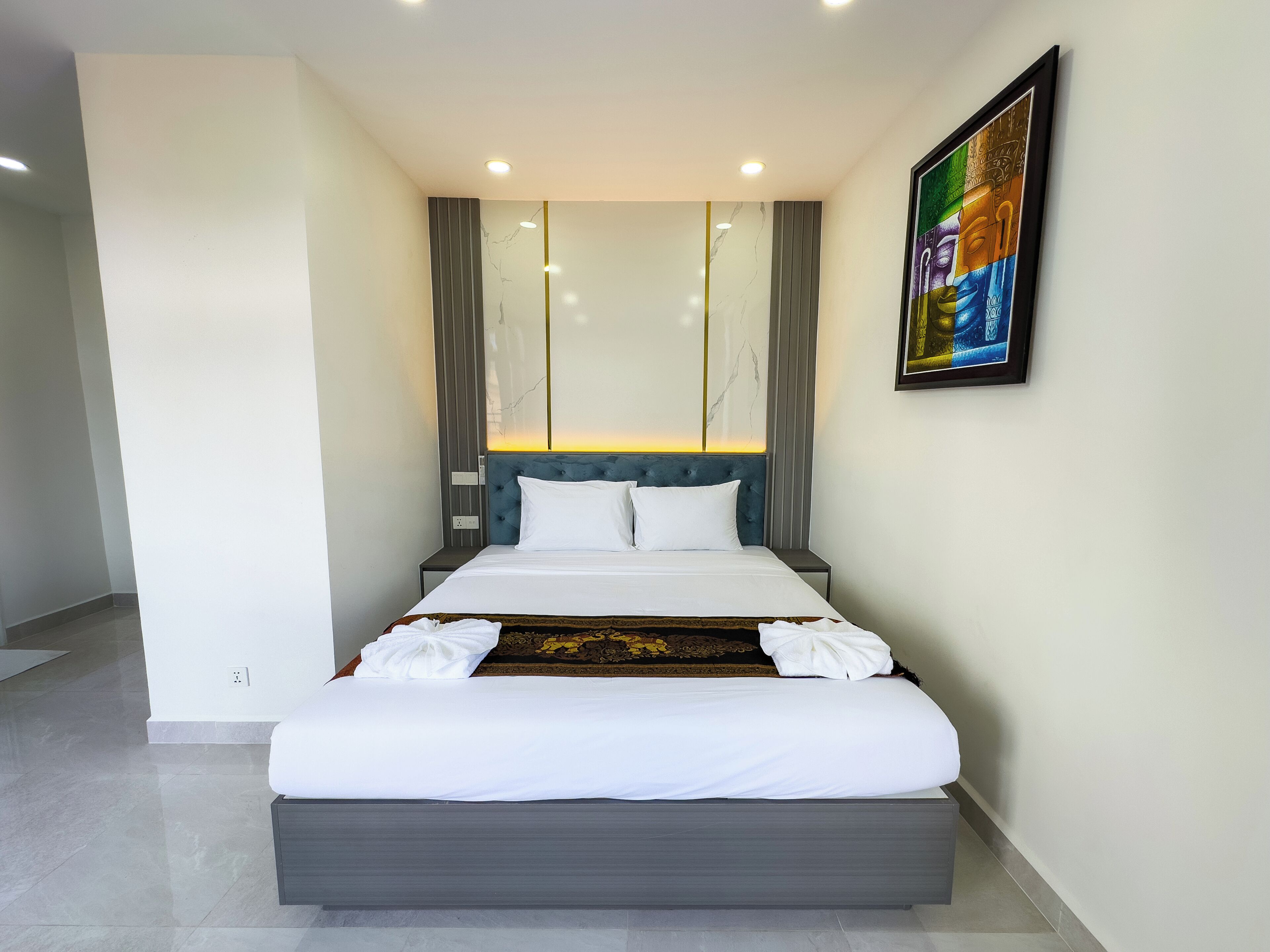 Una camera d'hotel moderna con un letto grande, una testiera con illuminazione integrata, un quadro appeso al muro e un design pulito e minimalista.