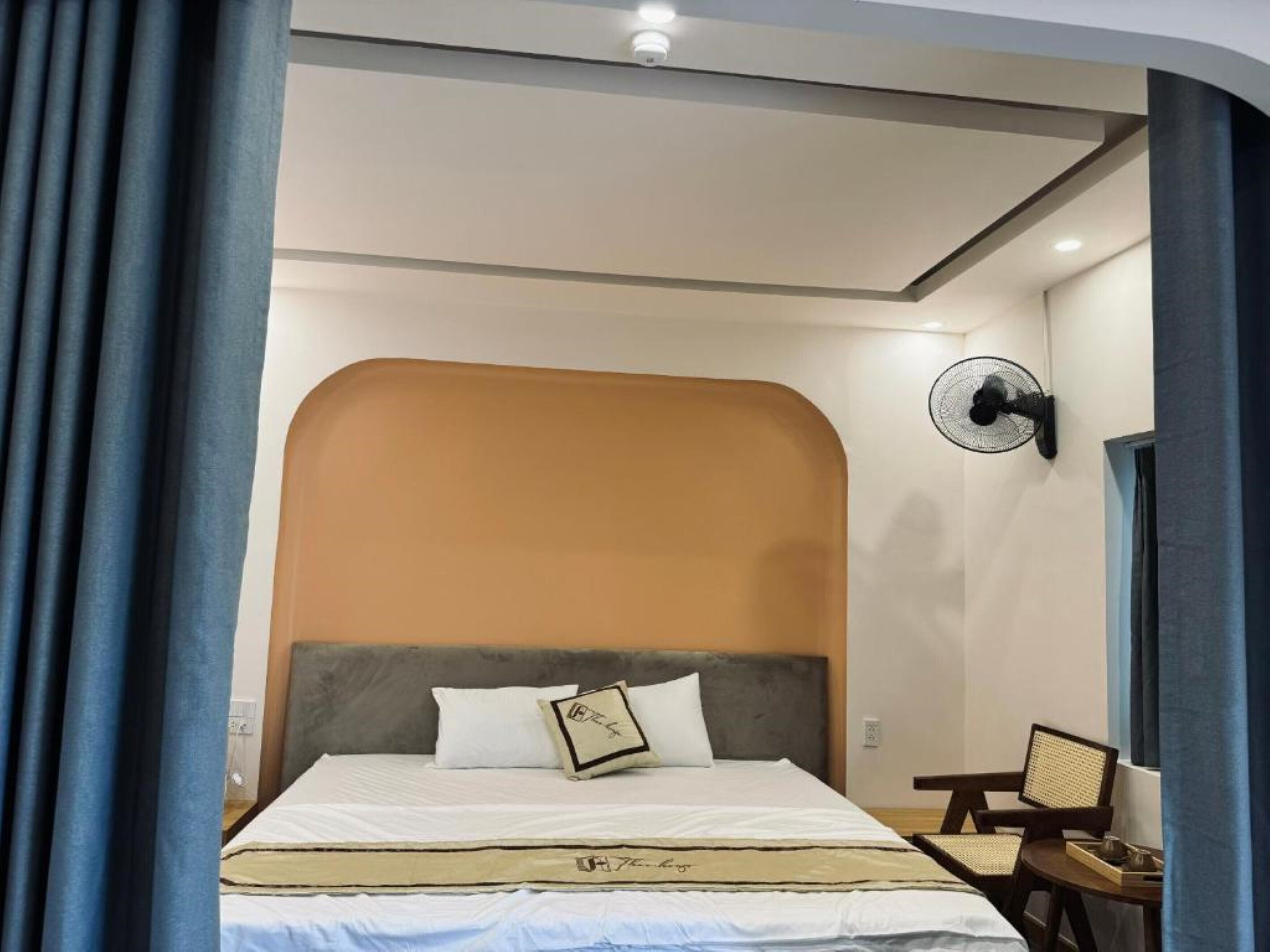 A hotel room with a bed, a wall clock, a fan, and a chair.